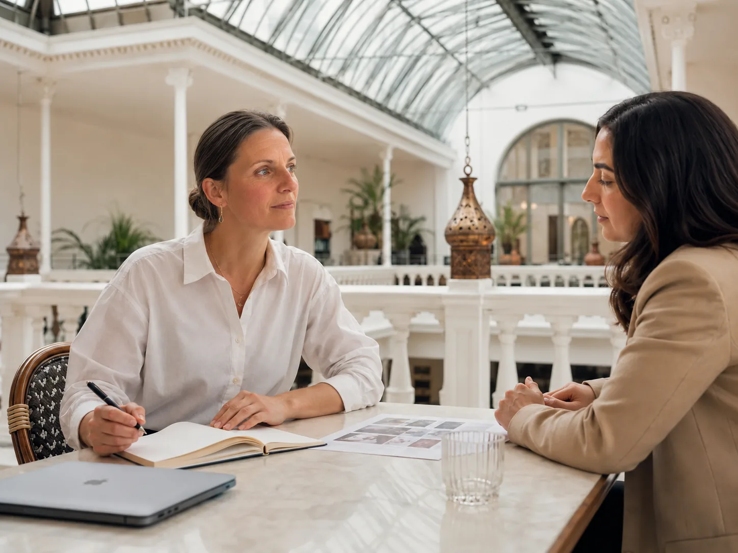 Zwei Frauen besprechen im Palmenhaus an einem Tisch ein Angebot.