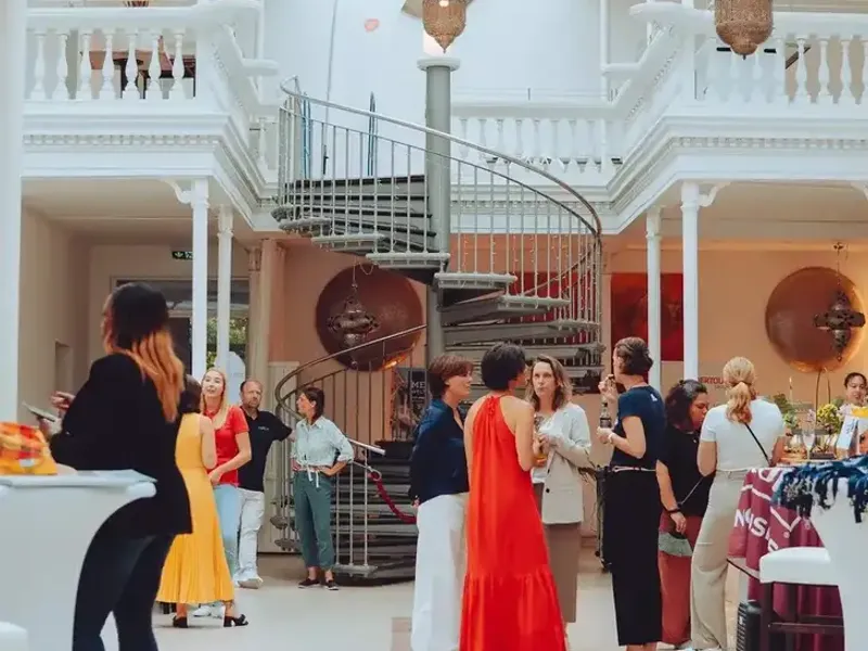 Abendveranstaltung im Palmenhaus Erfurt: Gäste im Gespräch an der Wendeltreppe, warmes Licht unter dem Glasdach.