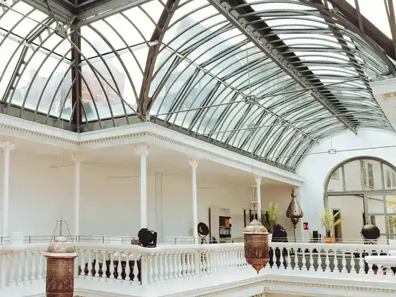 Innenraum des Palmenhauses Erfurt mit Glasdach, weißen Wänden, Balustrade und dekorativen Lampen.